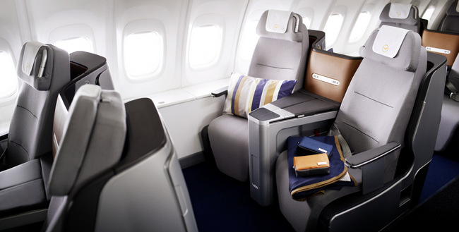 A pillow, a blanket and Lufthansa amenity kits are lying on the business class seats of a 747-8