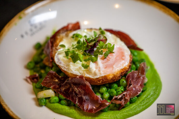 sautéed green peas topped with a fried egg and shaved Jamón ham