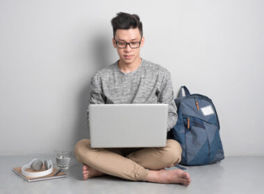 Young asian man in casual clothes is using a laptop, smiling while sitting on the floor