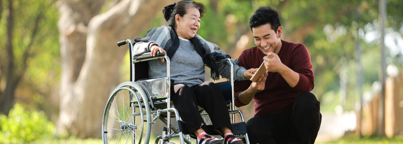 Asian senior woman sitting on the wheelchair with her son happy smile face on the green park (Depositphotos.com photo)