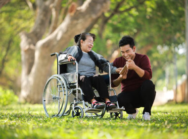 Asian senior woman sitting on the wheelchair with her son happy smile face on the green park (Depositphotos.com photo)