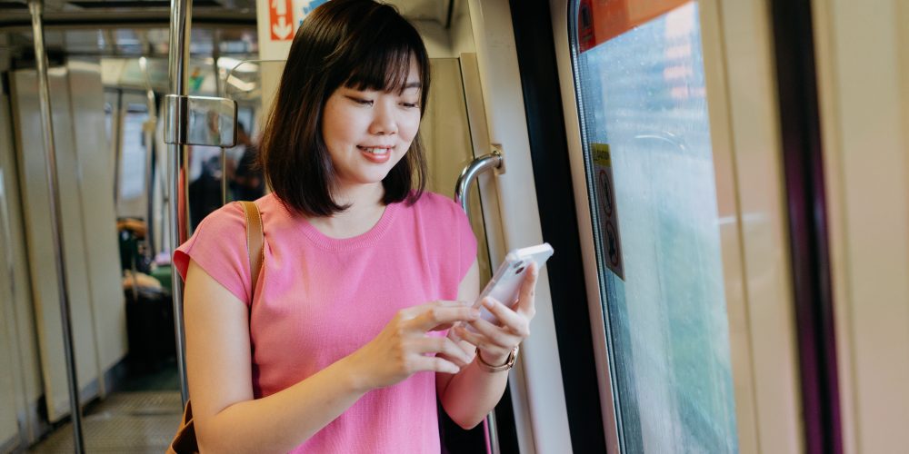 Young asian woman using smartphone while riding the train | SUPERADRIANME.com Young asian woman using smartphone while riding the train