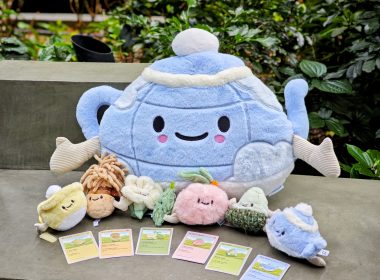 CHAGEE's six Bes-Tea Brew Crew plushies holding hands in front of a large blue Brew Pot Pillow Plush