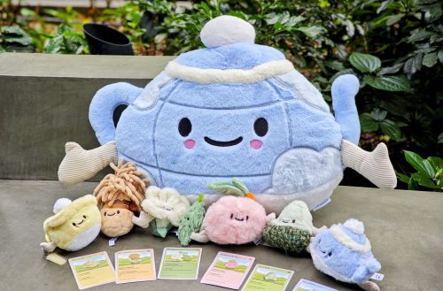 CHAGEE's six Bes-Tea Brew Crew plushies holding hands in front of a large blue Brew Pot Pillow Plush
